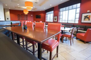 A restaurant interior with a long communal table, individual booths, and red upholstered chairs. - Drury Inn & Suites Columbus Grove City (Grove City)
