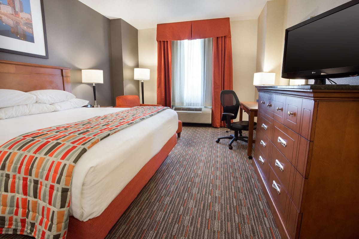 Ein Hotelzimmer mit einem großen Bett, einem Schreibtisch mit Stuhl, einem Fernseher und einer Kommode.