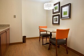 A dining area with a table and chairs, a trash can, and framed pictures on the wall. - Drury Inn & Suites Columbus Grove City (Grove City)