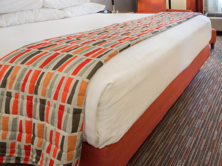 A hotel room with a large bed, two bedside lamps, a chair, and a framed picture on the wall.