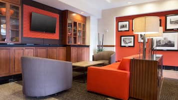 Un vestíbulo de hotel con una televisión de pantalla plana, armarios de madera, un sofá, una silla y una mesa.