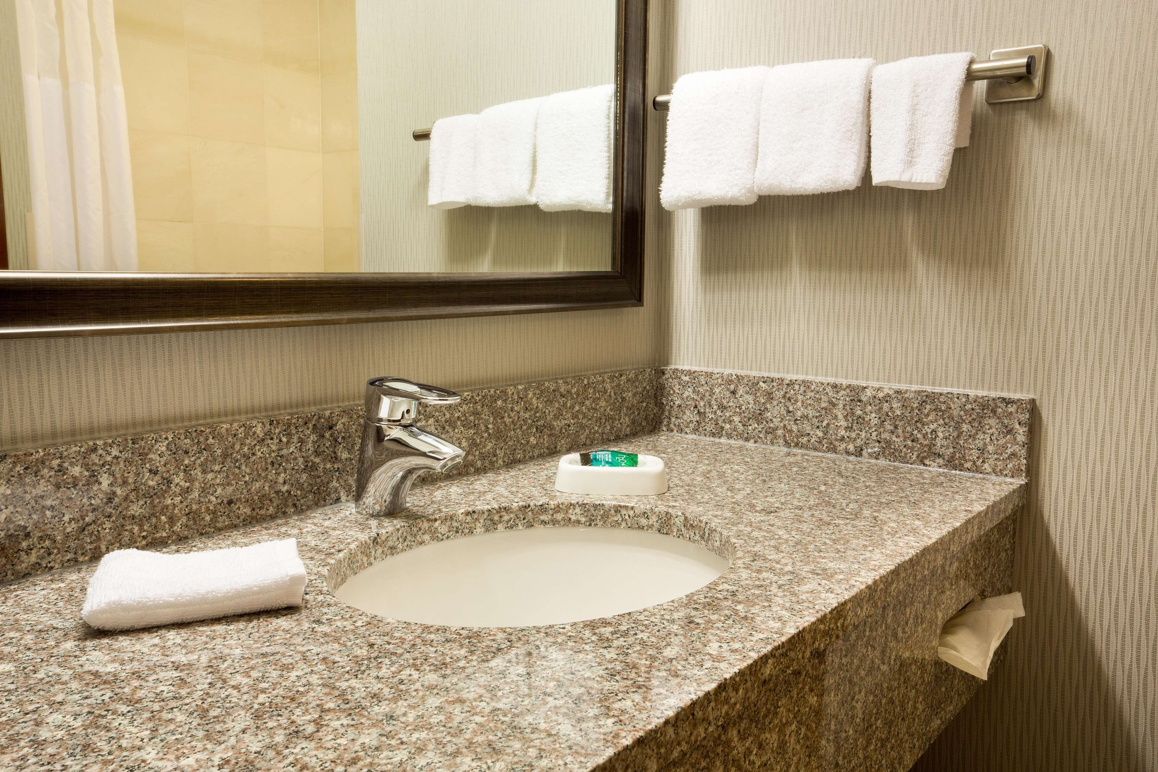 A bathroom with a granite countertop, a white sink, a mirror, and a towel rack with two white towels.
