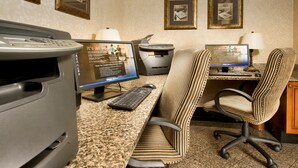 A hotel room with a desk, two computers, a printer, and two striped office chairs.