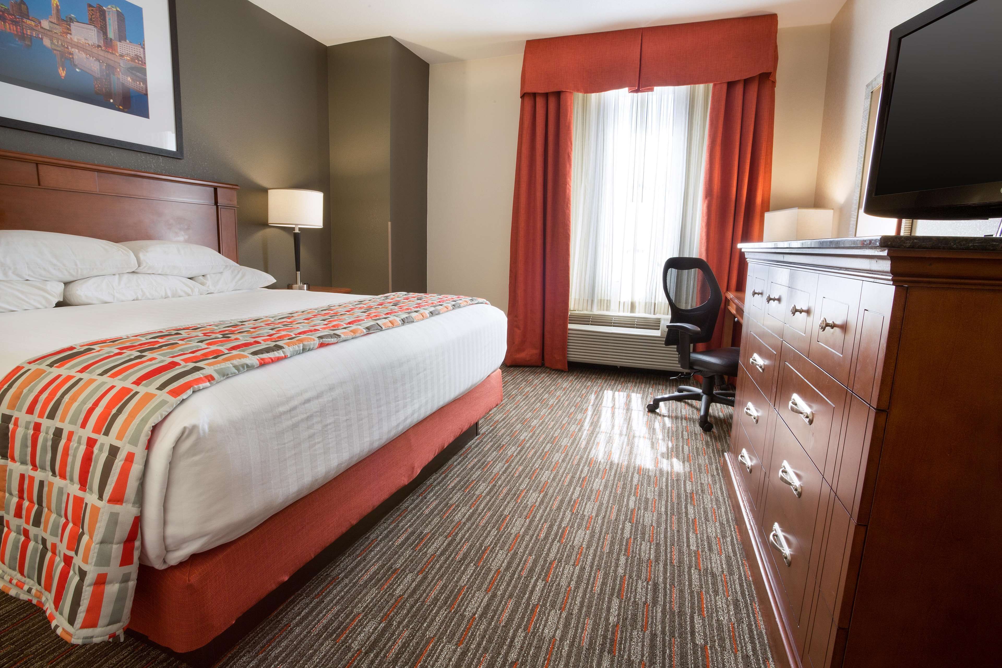 A hotel room with a bed, a desk, a chair, a television, and a window with curtains.