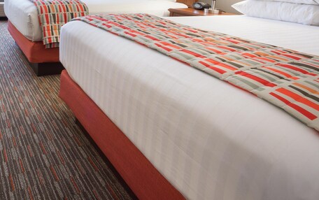 A hotel room with two beds, a red chair, a lamp, and a framed picture on the wall.