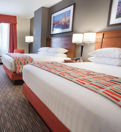 A hotel room with two beds, a red chair, a lamp, and a framed picture on the wall.