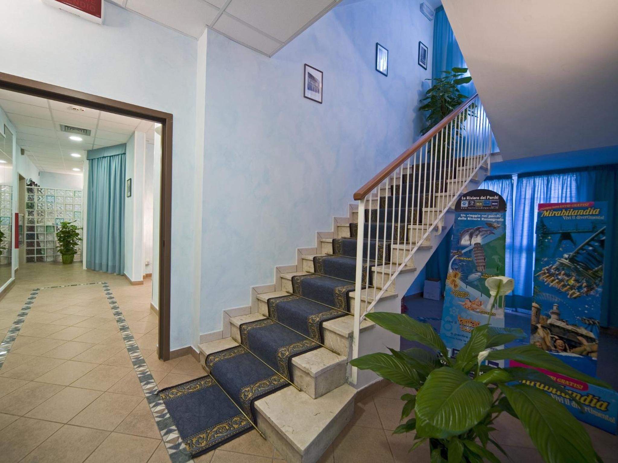 Un escalier dont les marches sont recouvertes d’une moquette bleue, menant à un palier ; un mur bleu orné d’une affiche et une plante sur le palier.