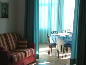 Ein Wohnzimmer mit einer Couch, einem Esstisch mit Stühlen und Vorhängen.