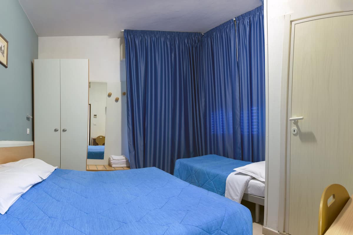 A hotel room with two beds, a wardrobe, a desk, and a bathroom visible through a curtain.