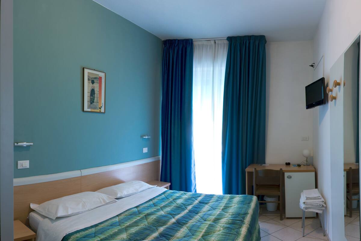 A hotel room with a bed, a desk, a TV, and a window with curtains.