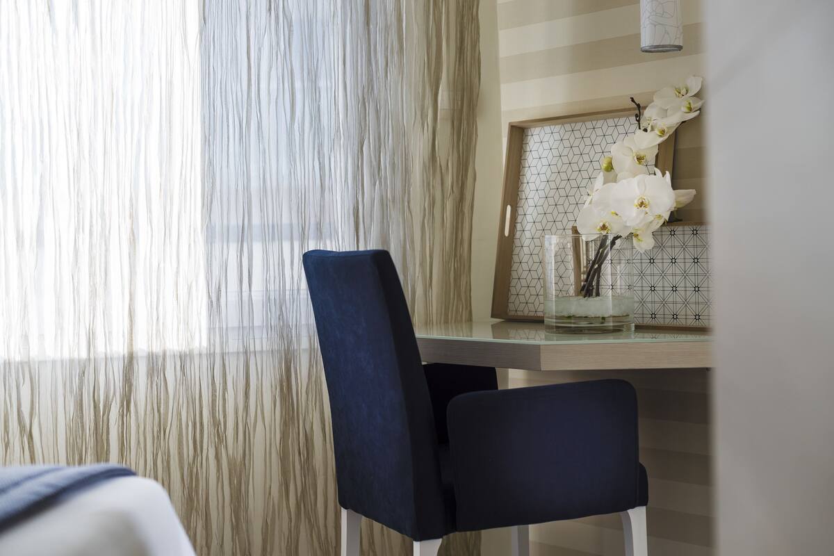 A modern dining area with a wooden table, two dark chairs, and a vase of white orchids.
