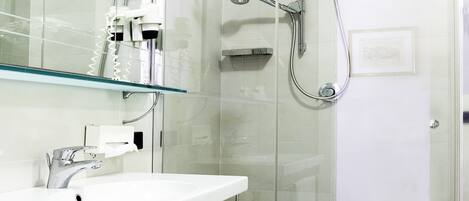 A modern bathroom with a glass-enclosed shower, a white sink with a mirror above, and a glass shelf.