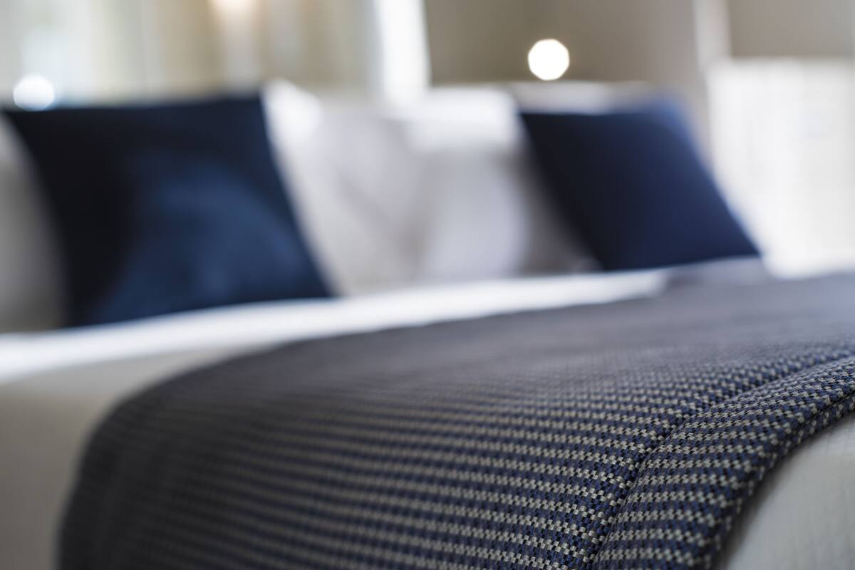 A close-up of a bed with a dark patterned bedspread and pillows in a hotel room.