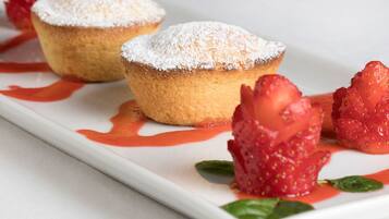A dessert plate with two muffins dusted with powdered sugar and strawberries.