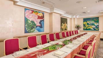 A long conference table with red chairs, white tablecloths, and floral centerpieces.