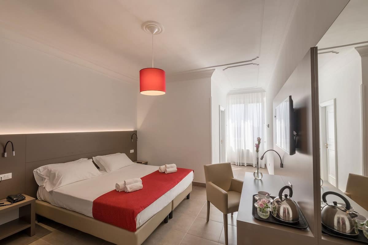 A hotel room with a bed, bedside table, desk, chair, and a TV mounted on the wall.