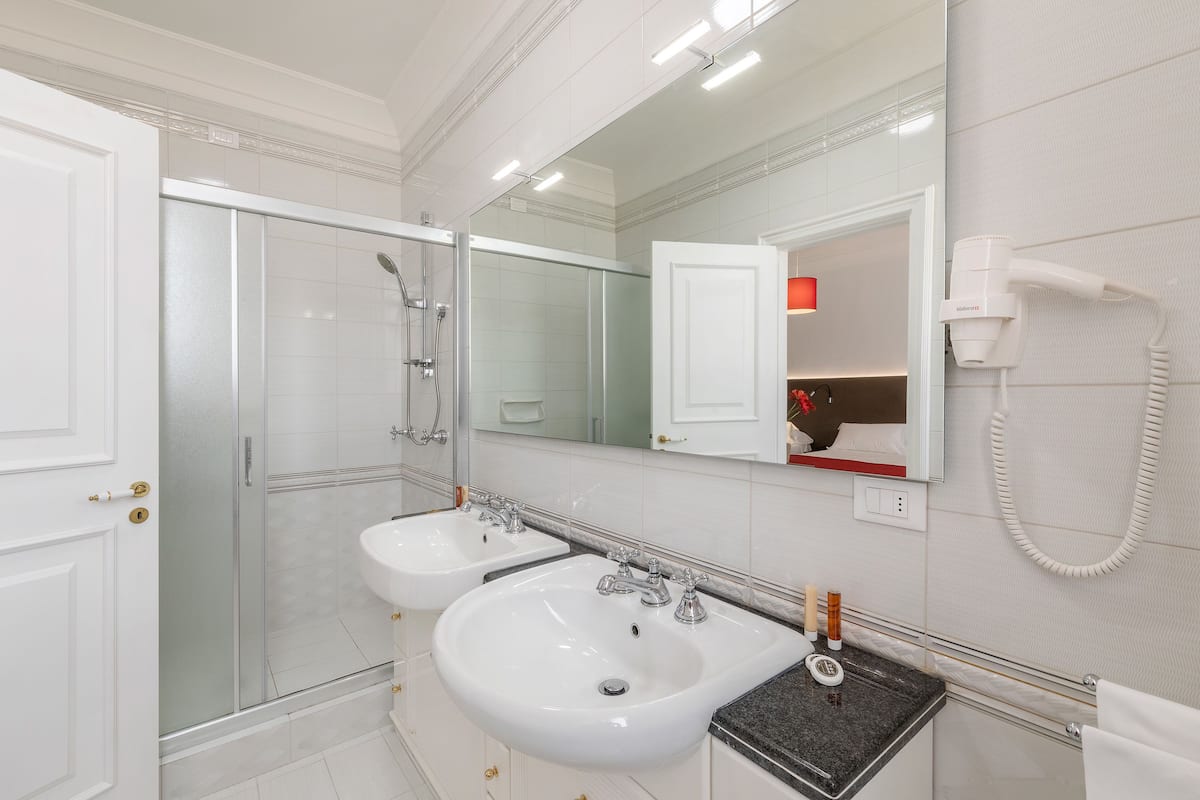 A modern bathroom with two sinks, a glass shower enclosure, a large mirror, and a hairdryer on the wall.