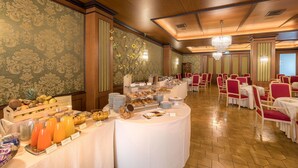 A buffet setup with various food items and beverages, surrounded by red and white chairs and tables. - Hotel Delle Palme (Lecce)
