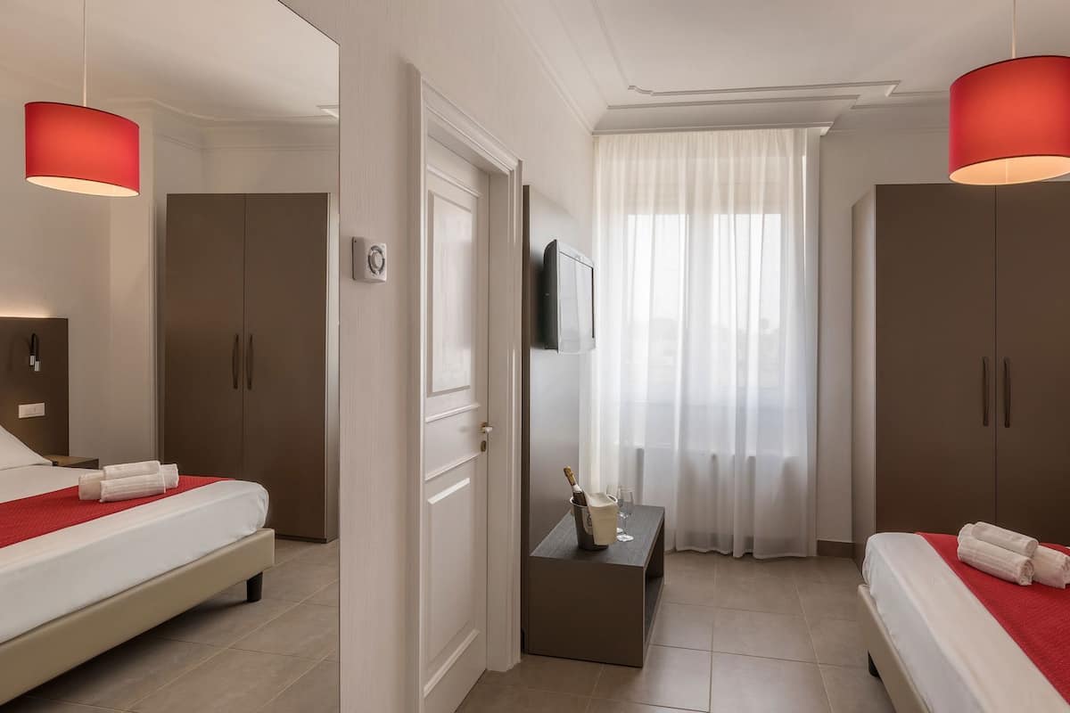 A hotel room with two beds, a TV, a minibar, and a window with curtains.