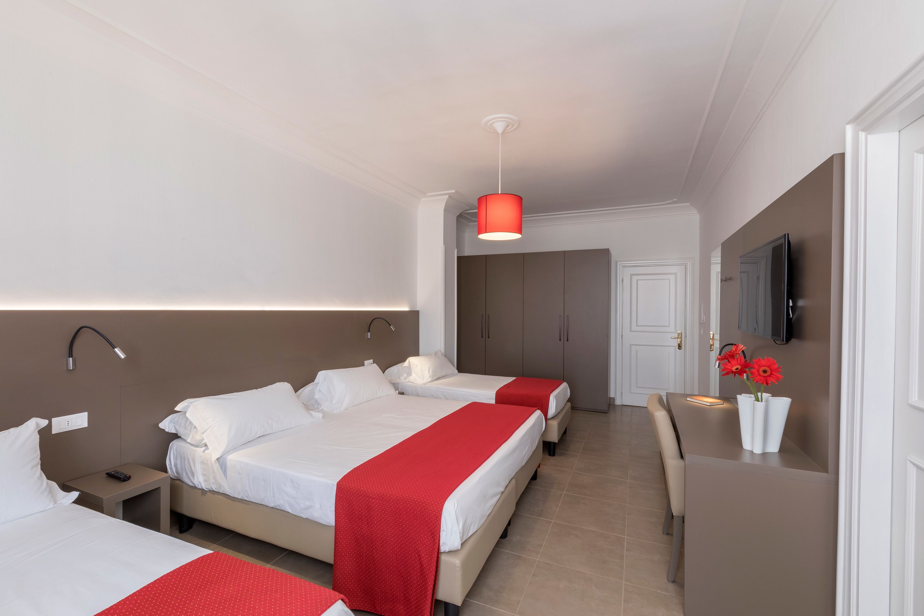 Ein Hotelzimmer mit zwei Betten, einem Schreibtisch, einem Fernseher und einer roten Pendelleuchte.