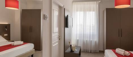 Habitación de hotel con dos camas, televisión, minibar y un amplio ventanal con cortinas.