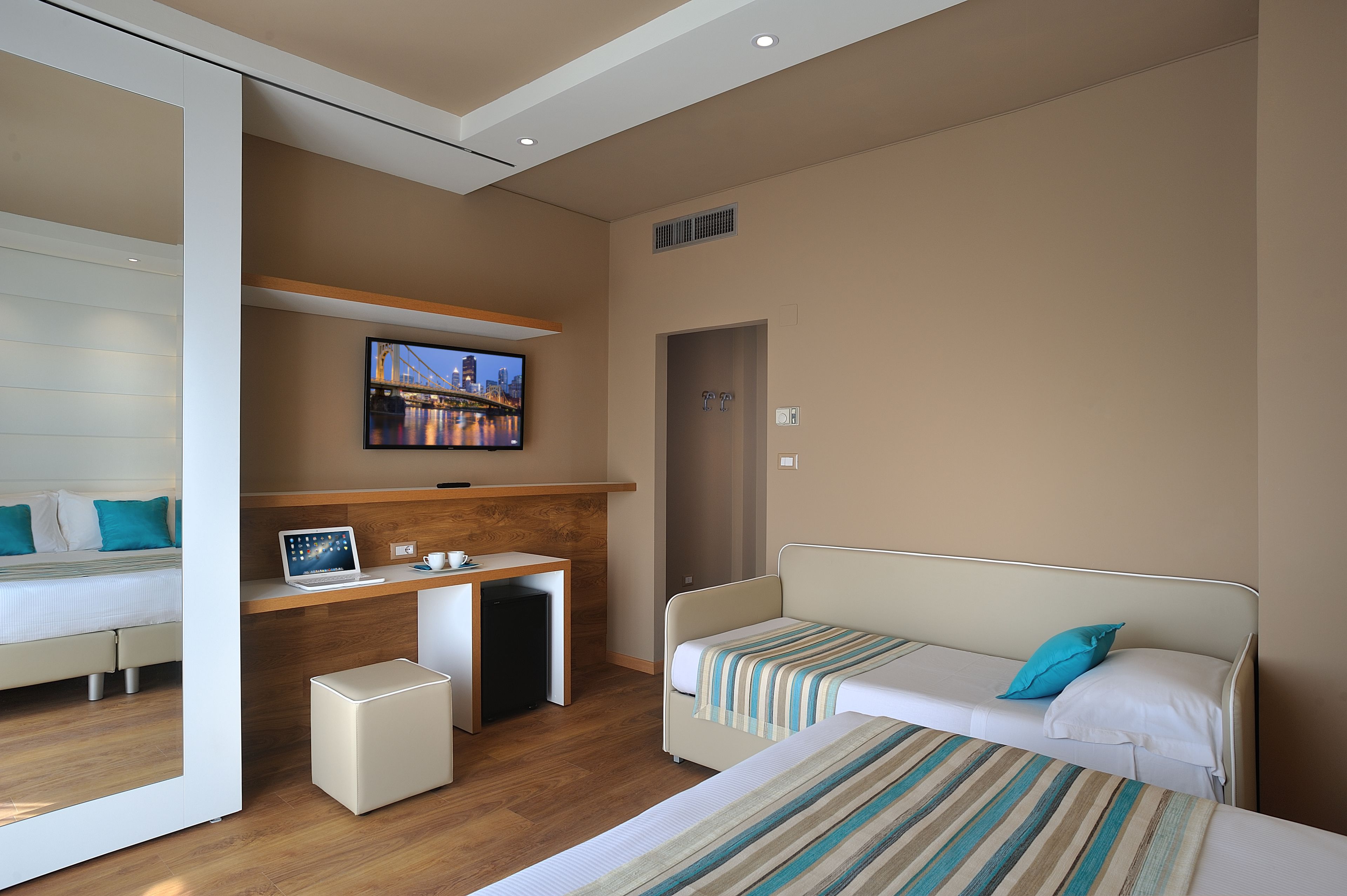 A modern hotel room with a bed, a desk, a TV, and a small seating area.