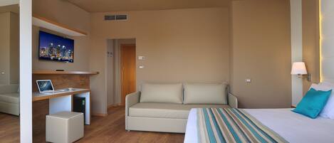 A modern hotel room with a bed, a sofa, a desk with a laptop, a TV, and a small cabinet.
