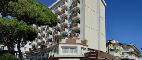 Un hotel de varios pisos con balcones, un cartel que dice 'CONCORD HOTEL' y zonas de estar al aire libre.