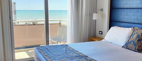 A hotel room with a large bed, a view of the beach, and a sliding glass door to the balcony.