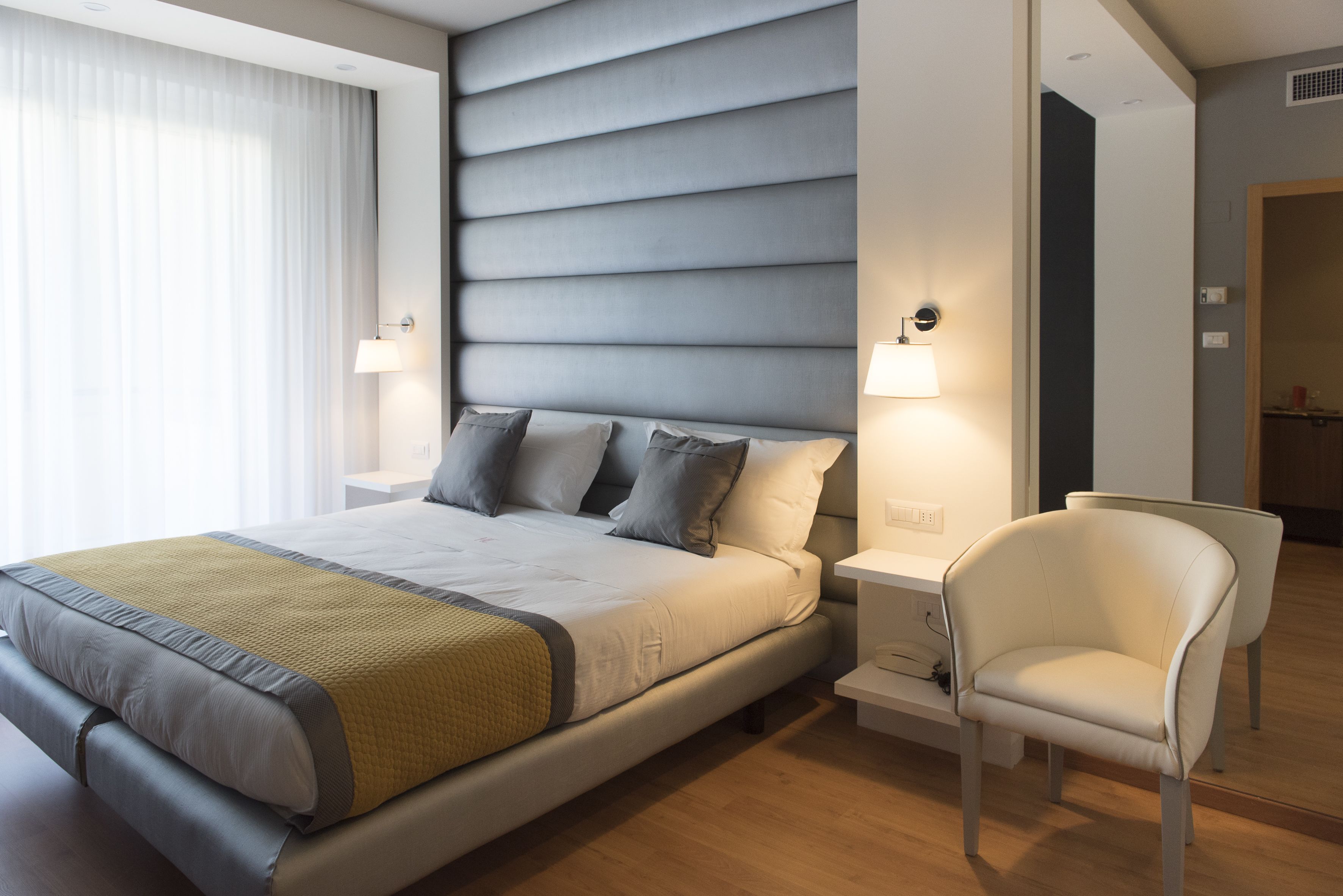Ein modernes Hotelzimmer mit einem großen Bett, Nachttischlampen, einem Sessel und Holzböden.