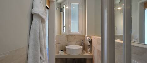 Un baño moderno con un lavamanos blanco, una cabina de ducha de vidrio y una toalla colgada en la pared.