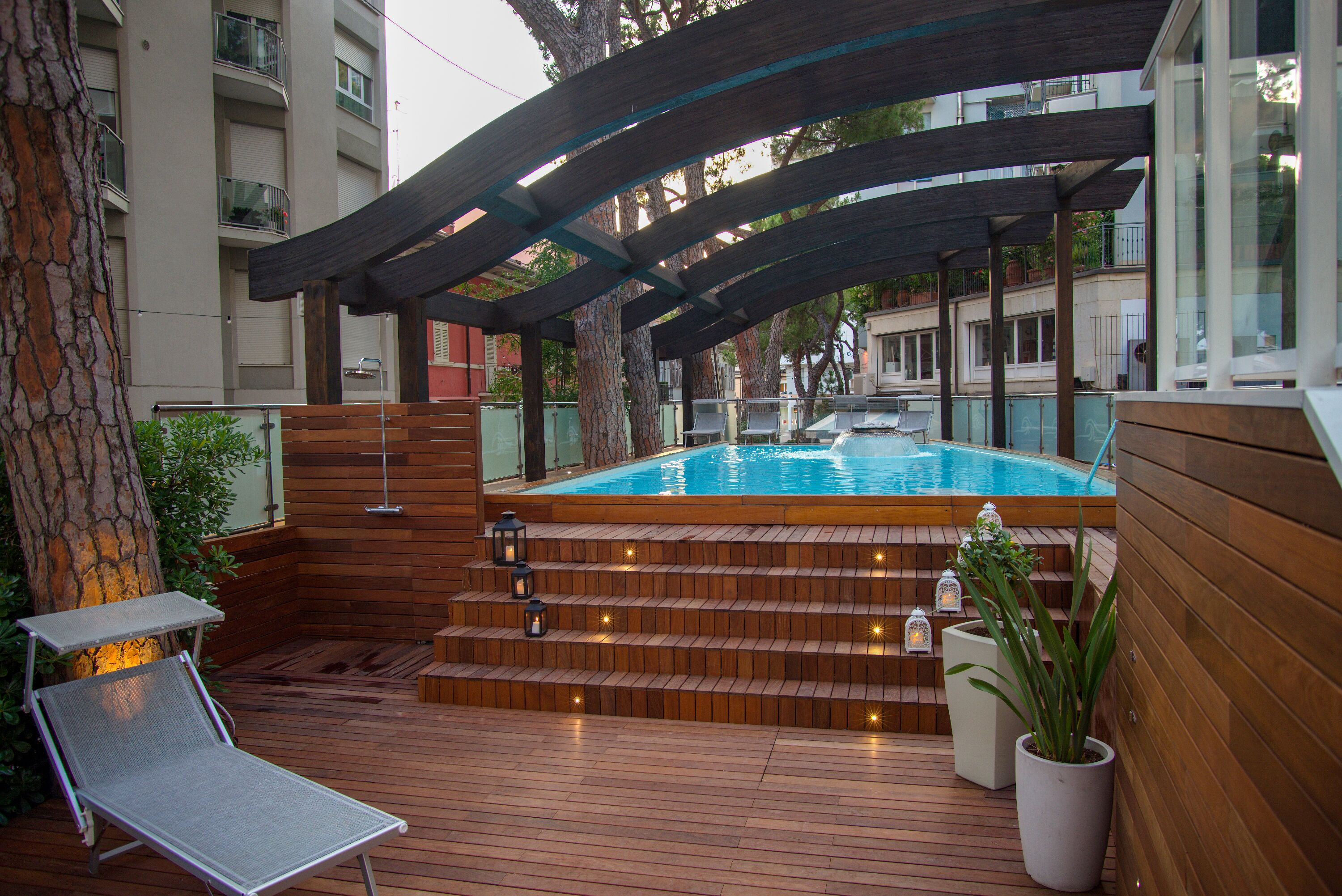 A wooden deck with a hot tub, lounge chairs, and steps leading to a pool.