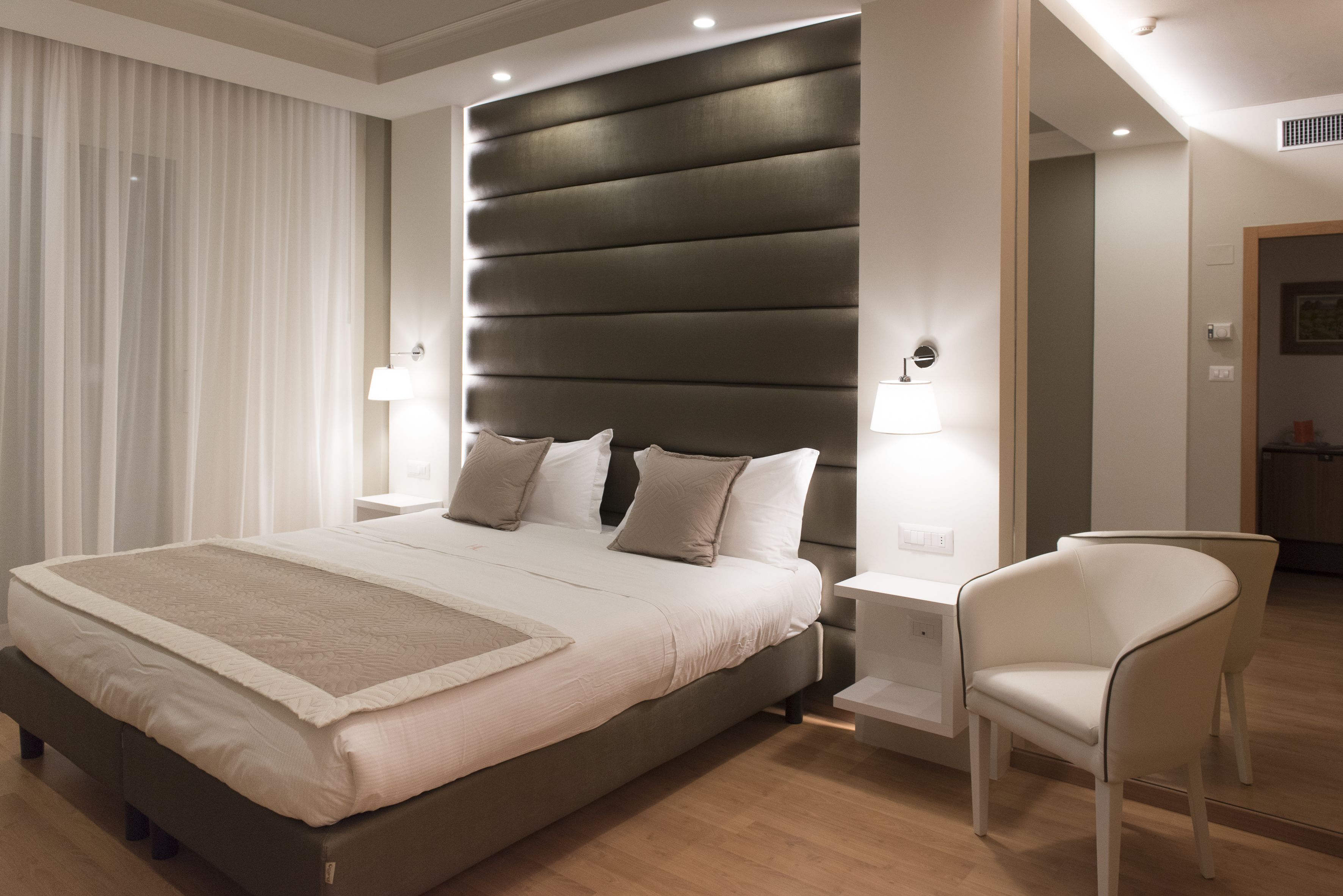 Un dormitorio moderno con una cama grande, lámparas de noche y una silla.