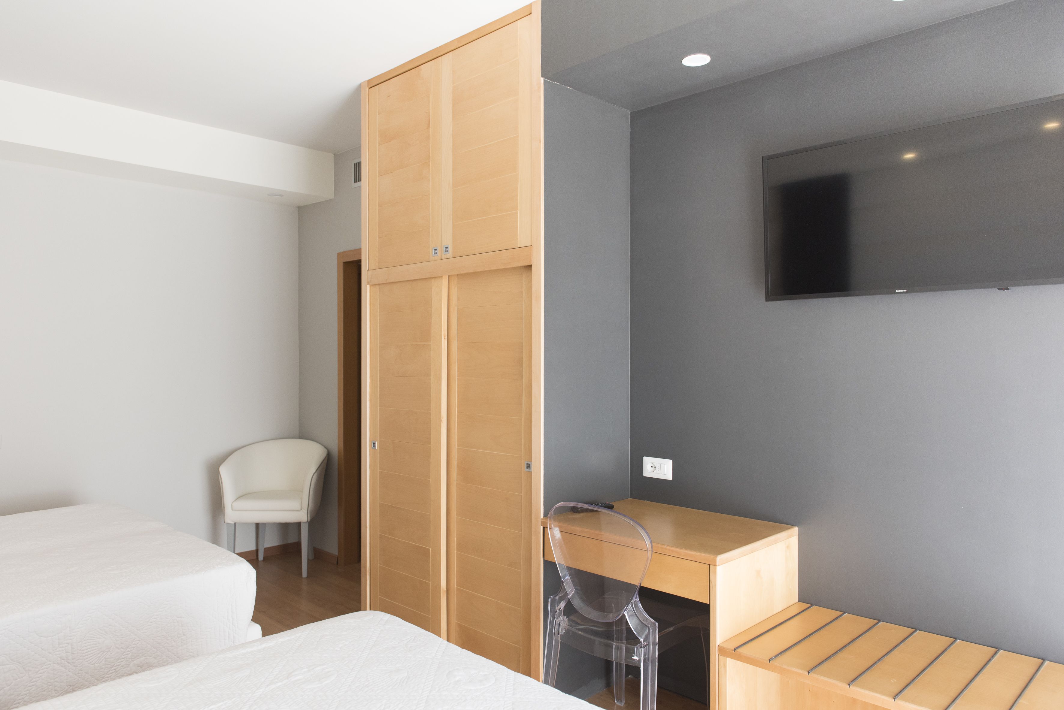 A hotel room with a bed, a desk, a chair, and a TV on the wall.