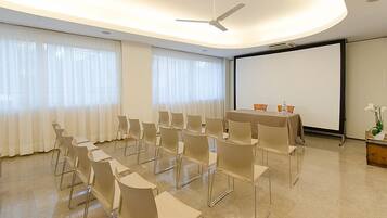 Ein Konferenzraum mit Tisch, Stühlen, einer Projektionsleinwand und einem Deckenventilator.