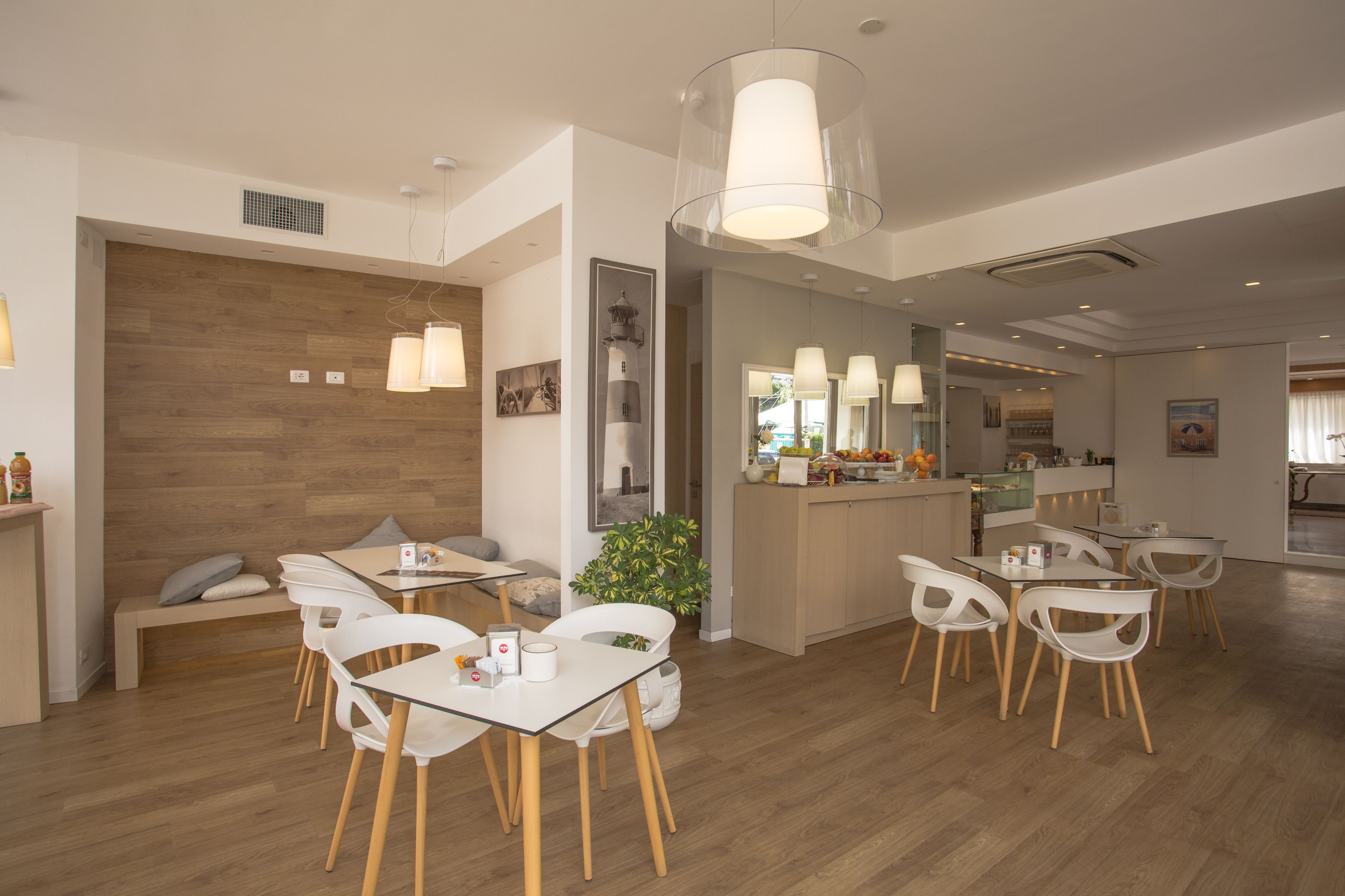 Un espace de restauration moderne avec des tables et des chaises blanches, un plancher en bois et des luminaires suspendus.