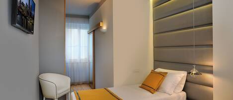 A modern bedroom with a bed, a chair, a bedside table, and a wall-mounted TV.
