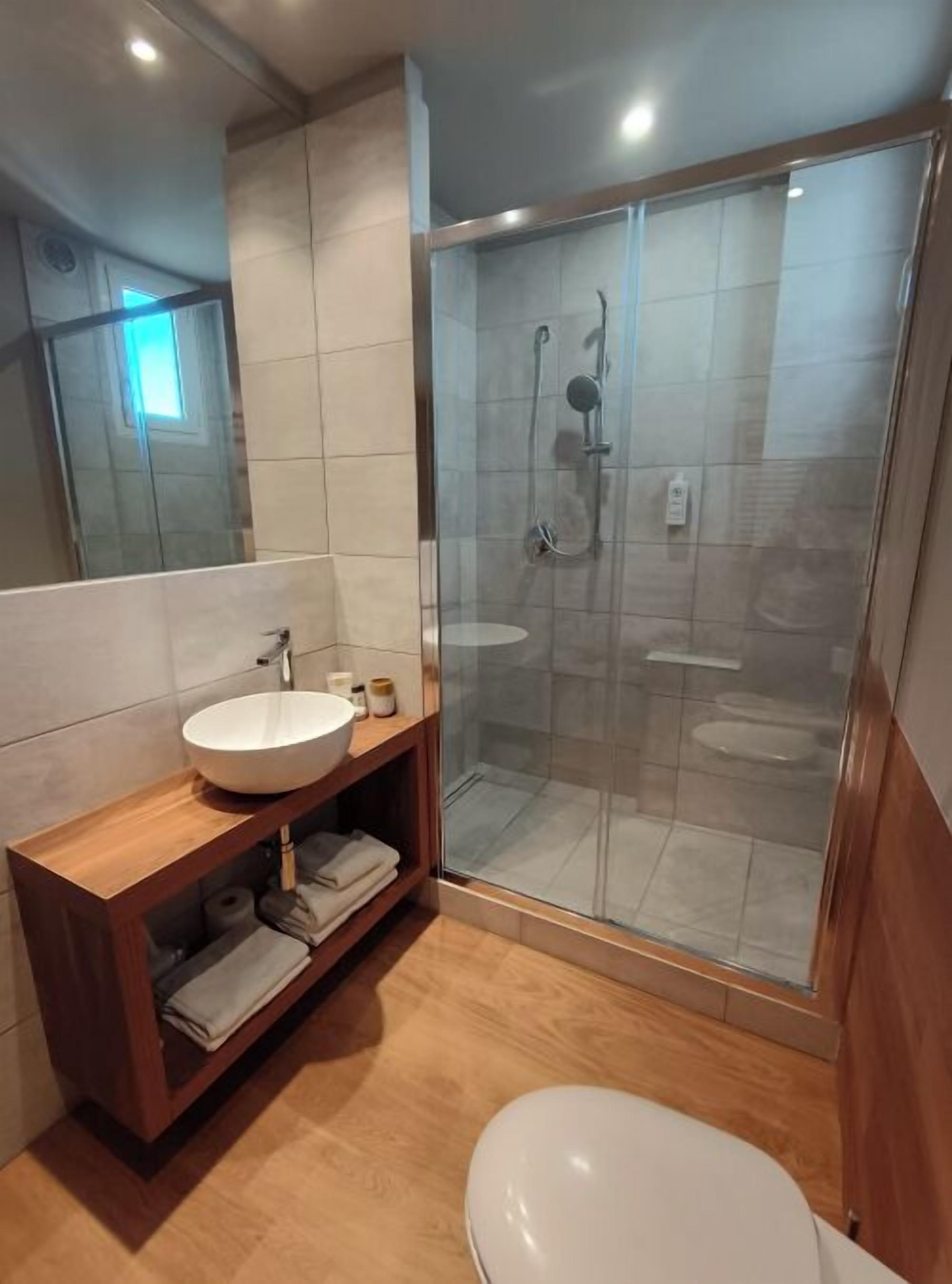 A modern bathroom with a glass-enclosed shower, a wooden vanity with a sink, and a toilet.