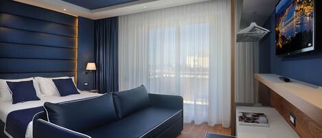 Habitación de hotel moderna con una cama grande, un sofá, un televisor montado en la pared y una mesita de noche de madera.