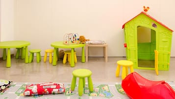 Un'area giochi per bambini con tavoli e sgabelli verdi, e una casetta.