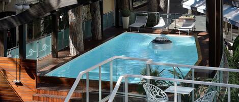 A rooftop pool area with a wooden deck, a small pool, and white lounge chairs.
