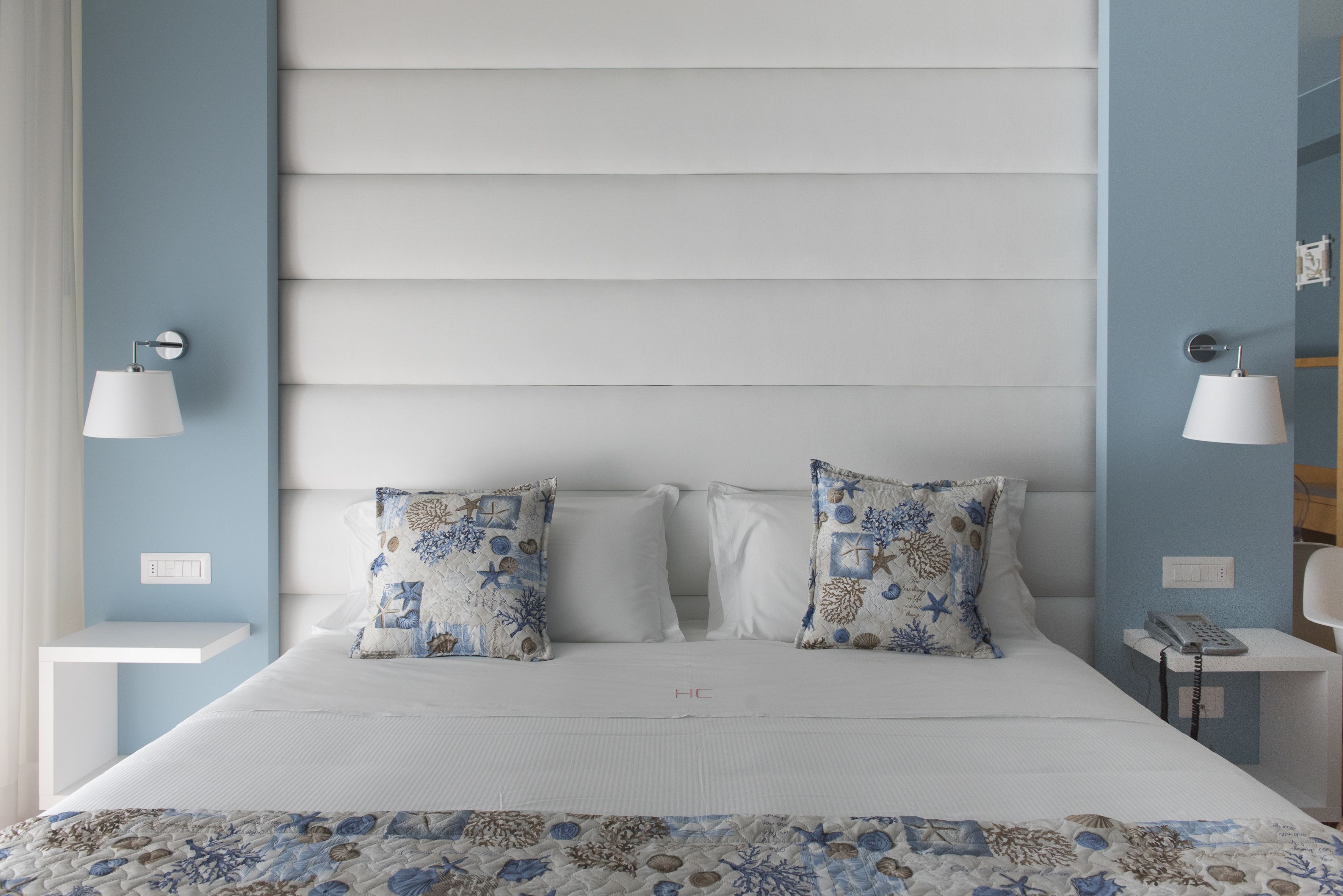 Une chambre à coucher avec un lit, deux coussins décoratifs, une table de chevet avec une lampe et un téléphone fixé au mur.