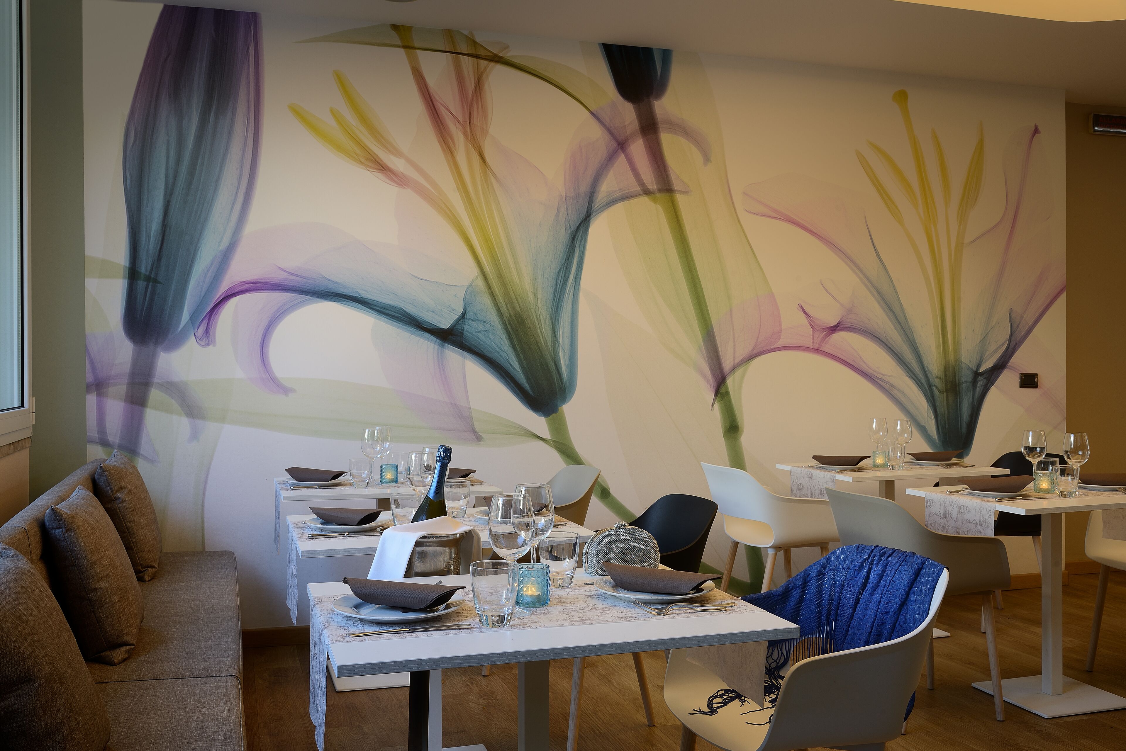 Un espace repas avec des tables dressées pour le repas, des chaises et un mur orné d’une fresque florale.