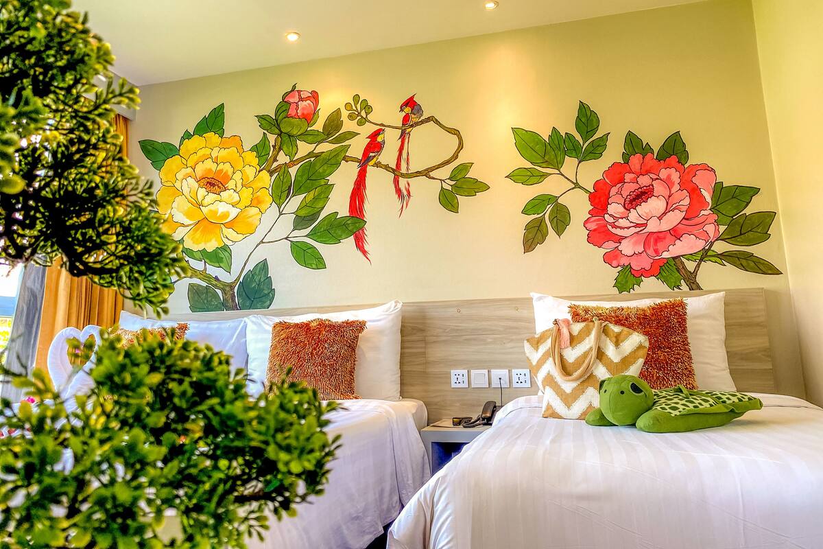Une chambre d’hôtel avec deux lits, une table de chevet et une fresque murale représentant des fleurs et des oiseaux.