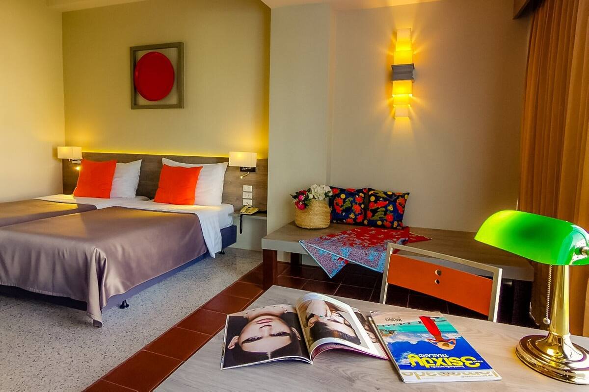 Une chambre d’hôtel avec un lit, des tables de chevet, un bureau avec une lampe et un magazine posé sur le sol.