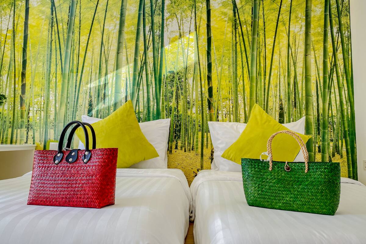 Une chambre d’hôtel avec deux lits, chacun étant équipé de draps blancs et d’oreillers jaunes. Deux sacs en tissu, l’un rouge et l’autre vert, sont posés sur les lits.