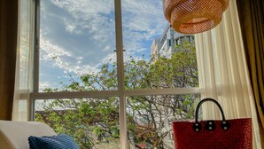 A room with a large window, a sofa with a blue pillow, a red woven bag on a chair, and a woven hanging light fixture. - Sino House Phuket Hotel (Phuket)
