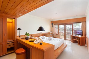 A hotel room with a wooden desk, two lamps, a telephone, a plant, a bed with white linens, a TV, and a balcony with a view. - Seaview Patong Hotel (Patong)