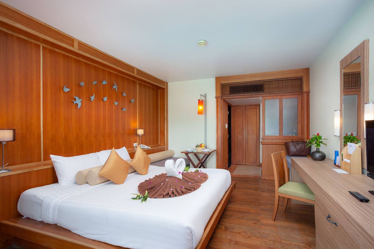 A hotel room with a wooden paneled wall, a bed with white bedding, a desk with a chair, and a mirror.