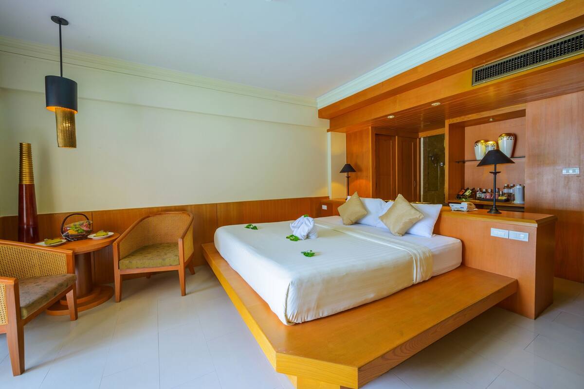 A hotel room with a large bed, a wooden desk, a chair, and a small table with a basket.
